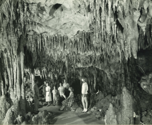 historical black and white photo of a group of young adults exploring an underground cave with stalagtites and stalagmites reach from the floor and ceiling